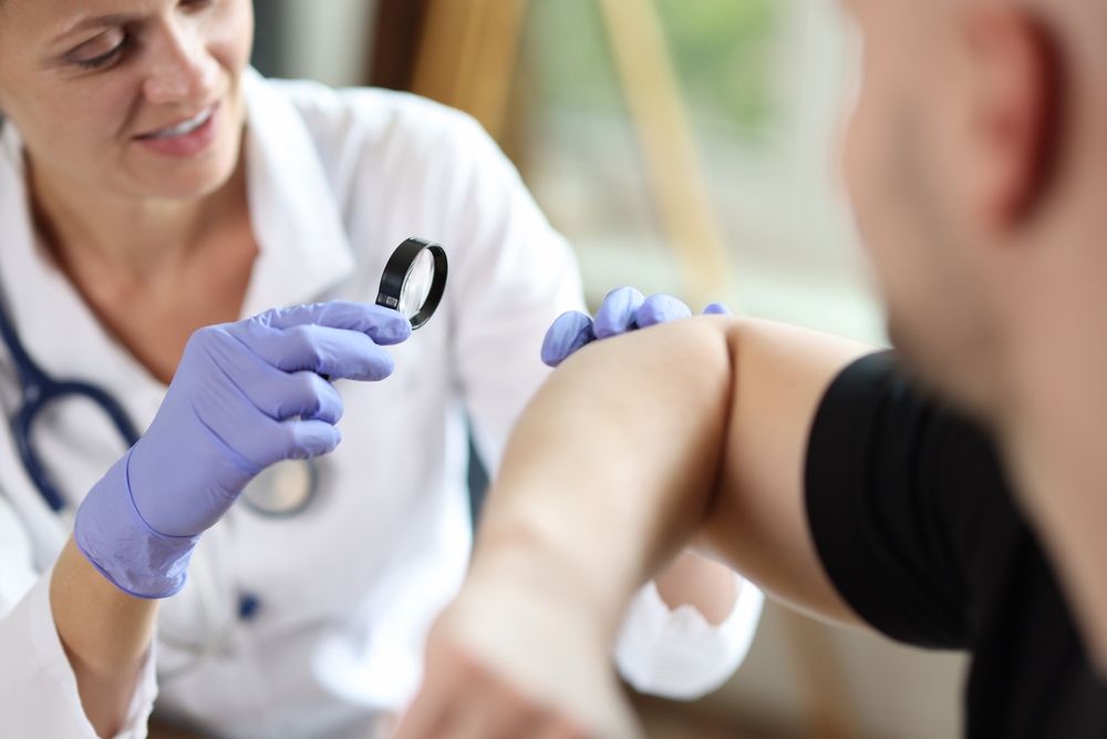 Dermatologist inspecting spot on man’s arm in for preventative dermatology appointment.